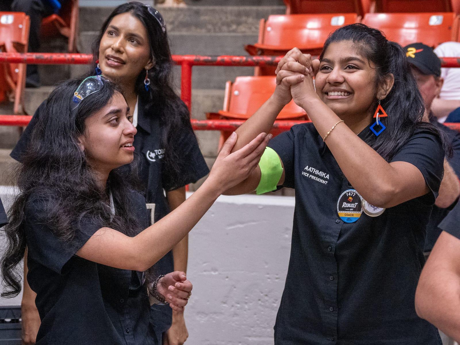 Three students celebrating in the stands at the FIRST Robotics Competition District Championship