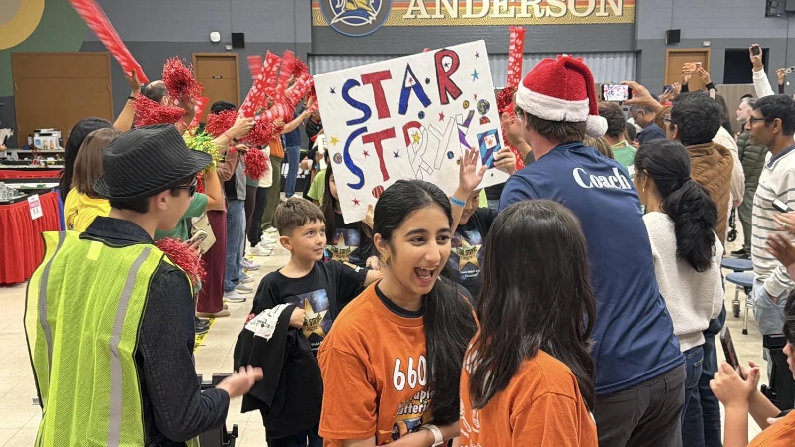 A FIRST LEGO League team in orange shirts celebrating with their Star Strike sign at a Texas qualifier